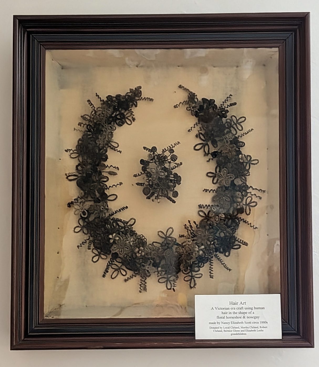 Framed hair art: a floral horseshoe and nosegay woven from human hair