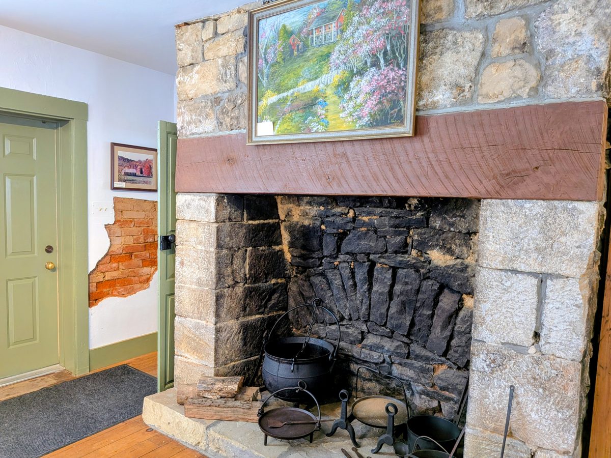 Inside the Wagner/Bentel Haus: a stone cooking hearth with iron kettles, a painting above the mantel