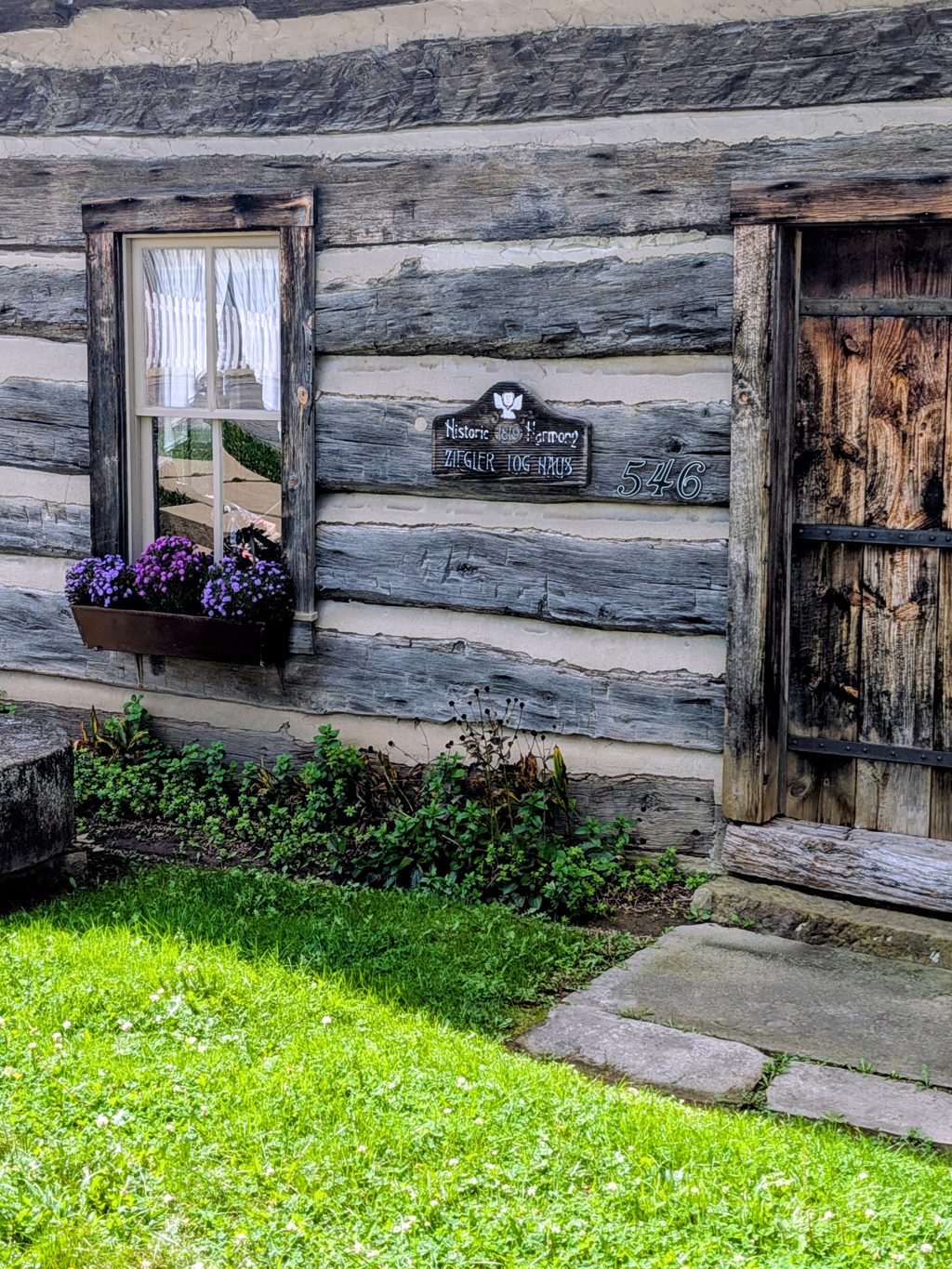 The Ziegler Log House: weathered log walls, a window box of purple flowers and the house sign