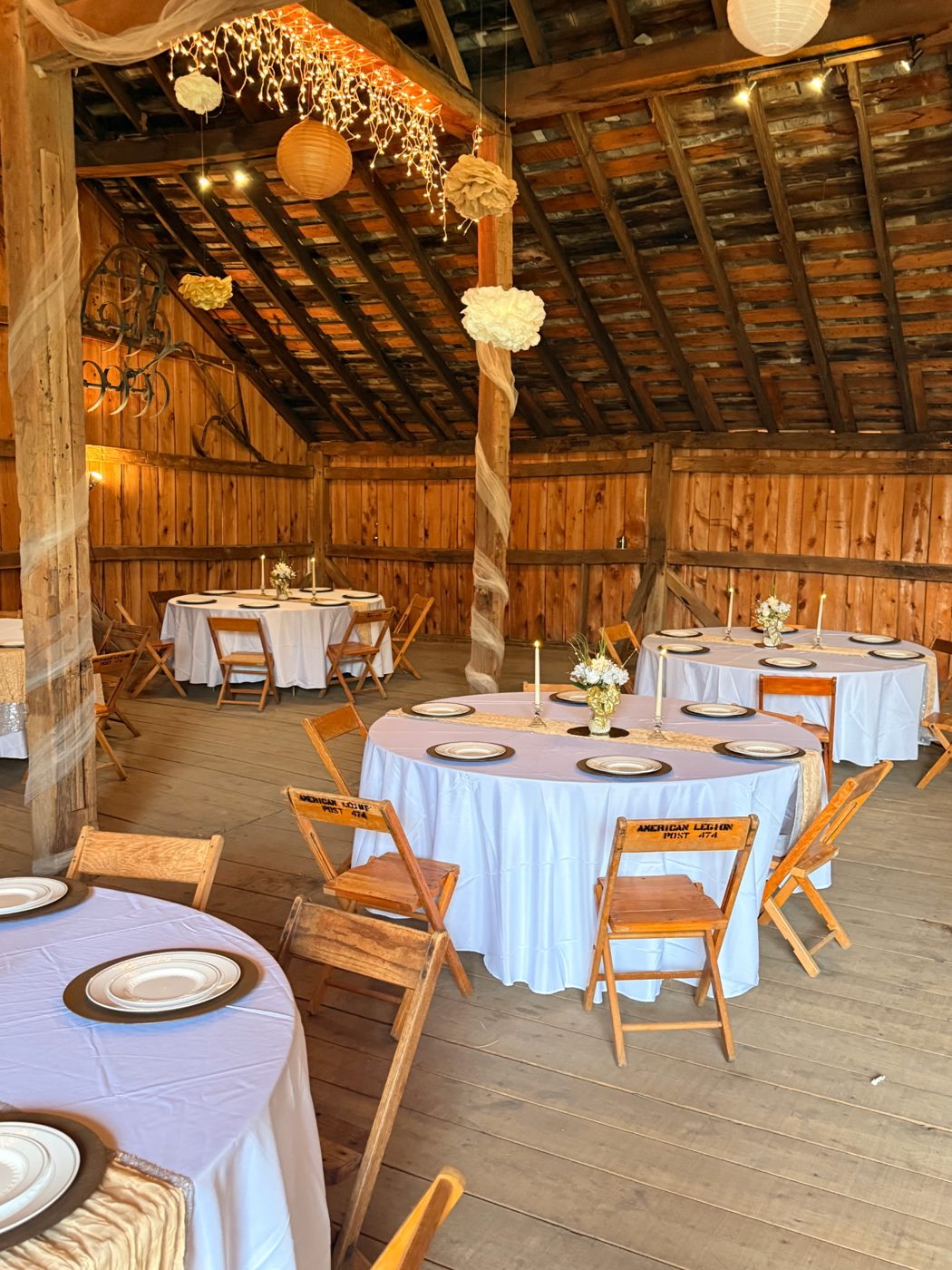 Inside the 1805 Harmonist Barn: round tables in white linen, candles and flowers, paper lanterns and lights hung from the rafters