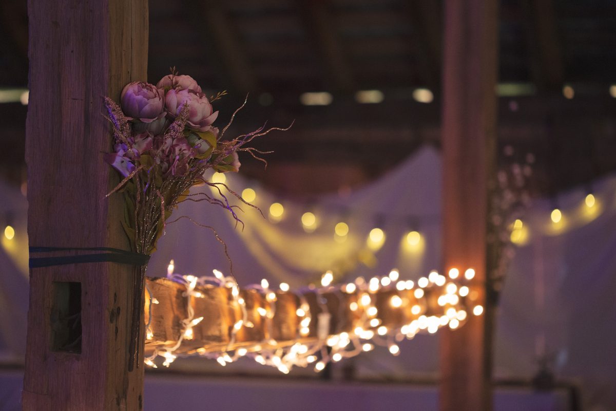 Flowers tied to a beam in the 1805 Harmonist Barn, with string lights glowing behind