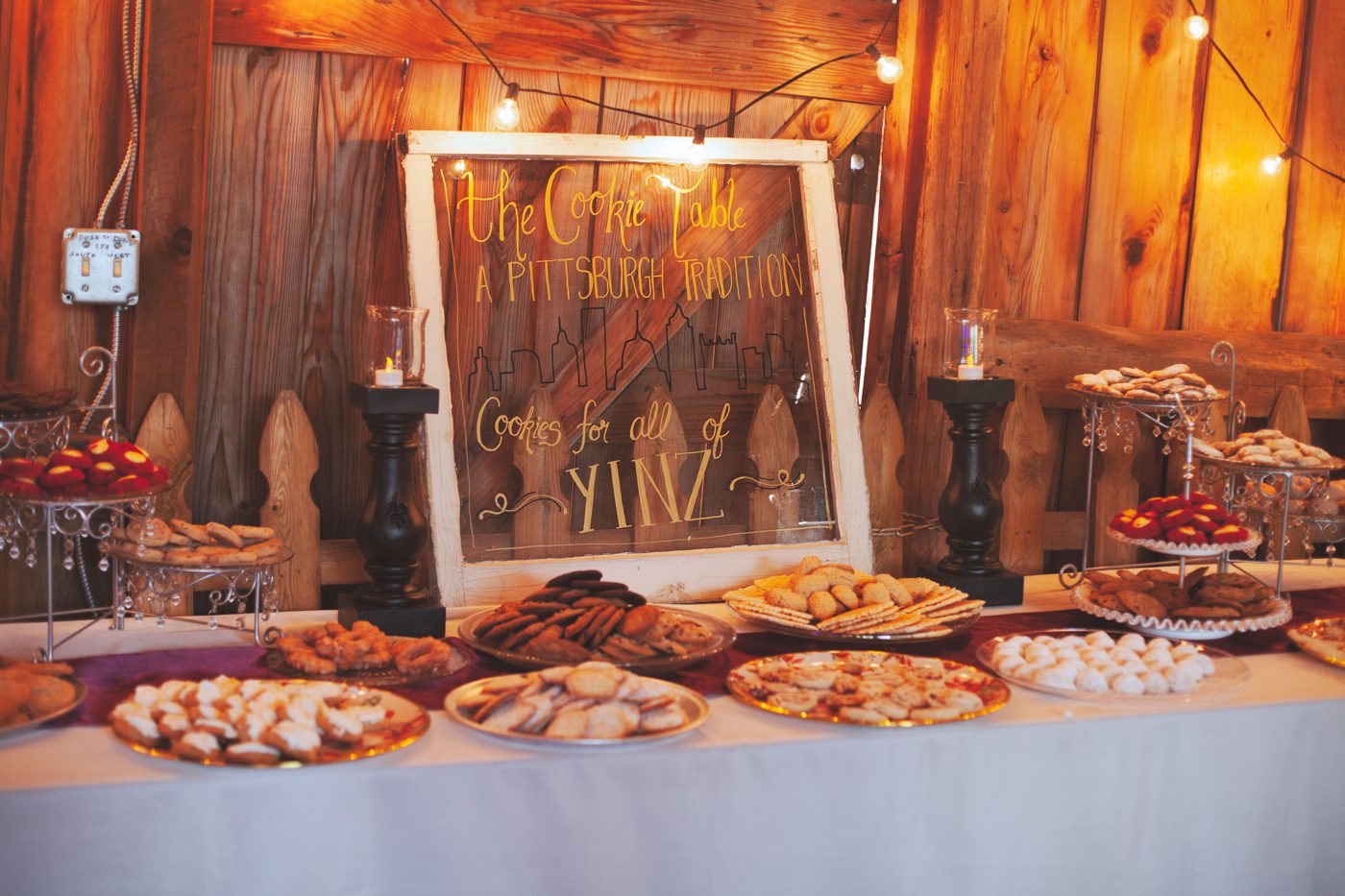 A Pittsburgh cookie table at a wedding in the barn, under string lights