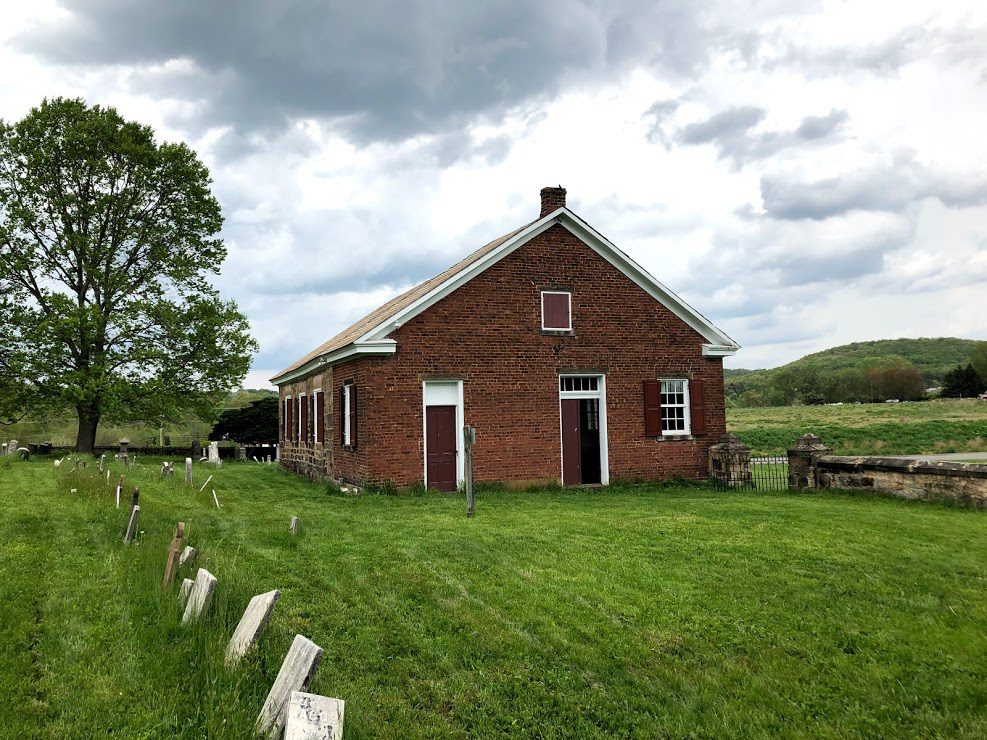 The 1825 Mennonite Meetinghouse, brick and stone under a big sky, with the old cemetery in front