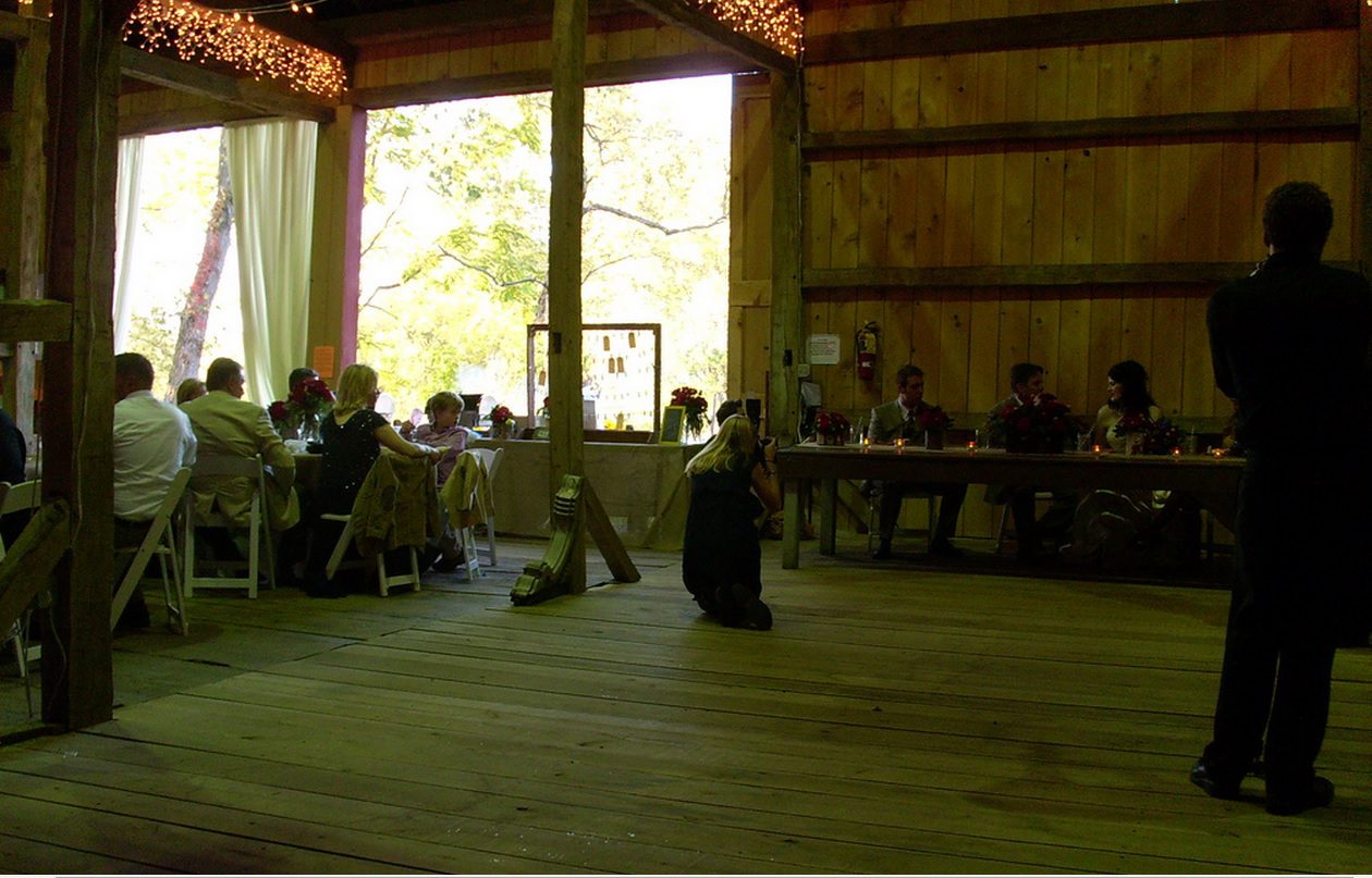 A wedding reception under strings of lights inside the 1805 Harmonist Barn, the doors open to the trees